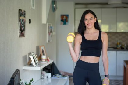 Smiling woman in activewear lifting dumbbells at home for a healthy lifestyle.