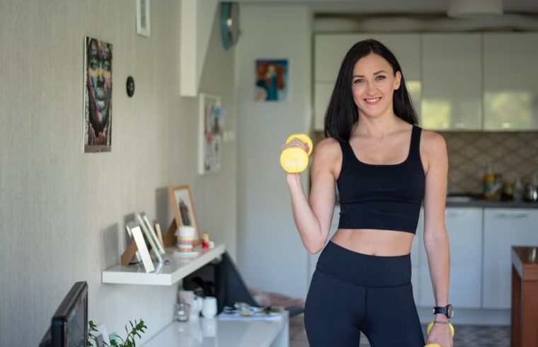 Smiling woman in activewear lifting dumbbells at home for a healthy lifestyle.